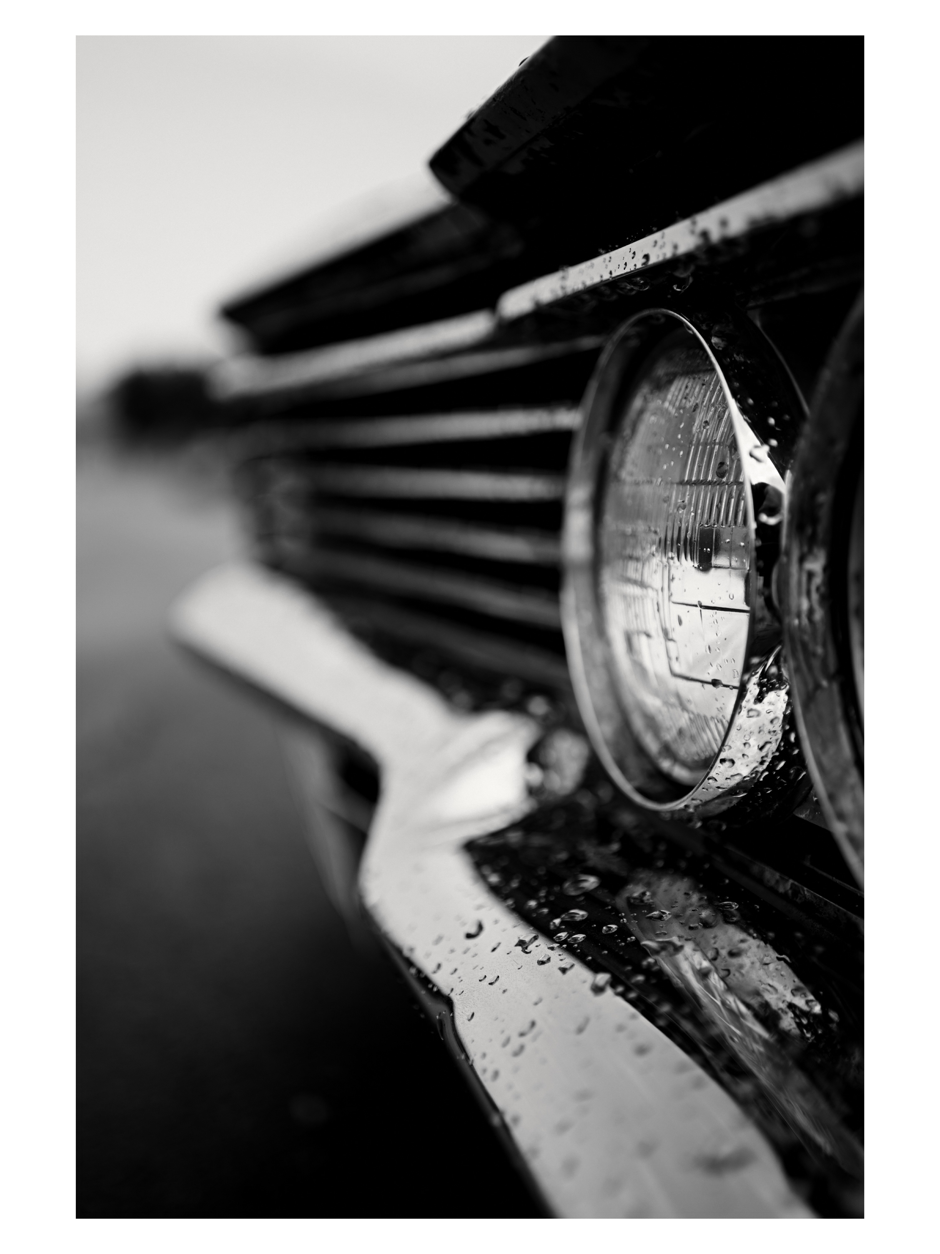 Rain-covered headlight and grille of a classic car photographed by Tony Shepherd